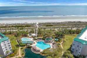 Ein Resort mit mehreren Schwimmbecken, Blick auf den Strand und einer angelegten Grünfläche mit Palmen.