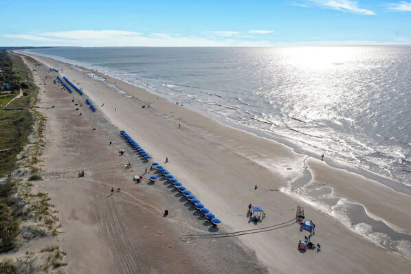 A beach with a long row of blue umbrellas and beach chairs, a sandy shore, and the ocean.