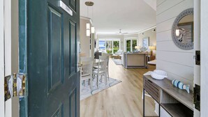 Een moderne hotelkamer met een donkerblauwe deur, een zithoek met een witte tafel en stoelen, en een keuken met een aanrecht en een decoratieve spiegel.