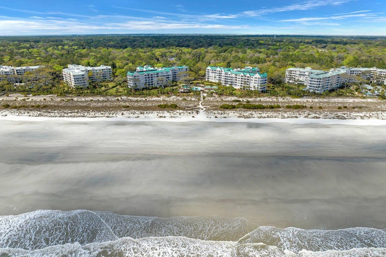 Un hotel frente a la playa con varias edificaciones, una playa de arena y vista al océano.
