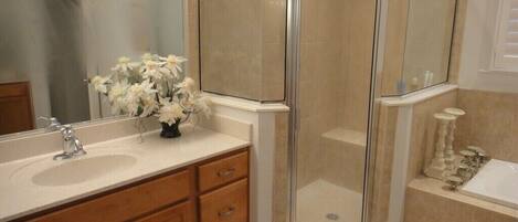 A bathroom with a glass-enclosed shower, a sink with a mirror, and a vase of flowers.