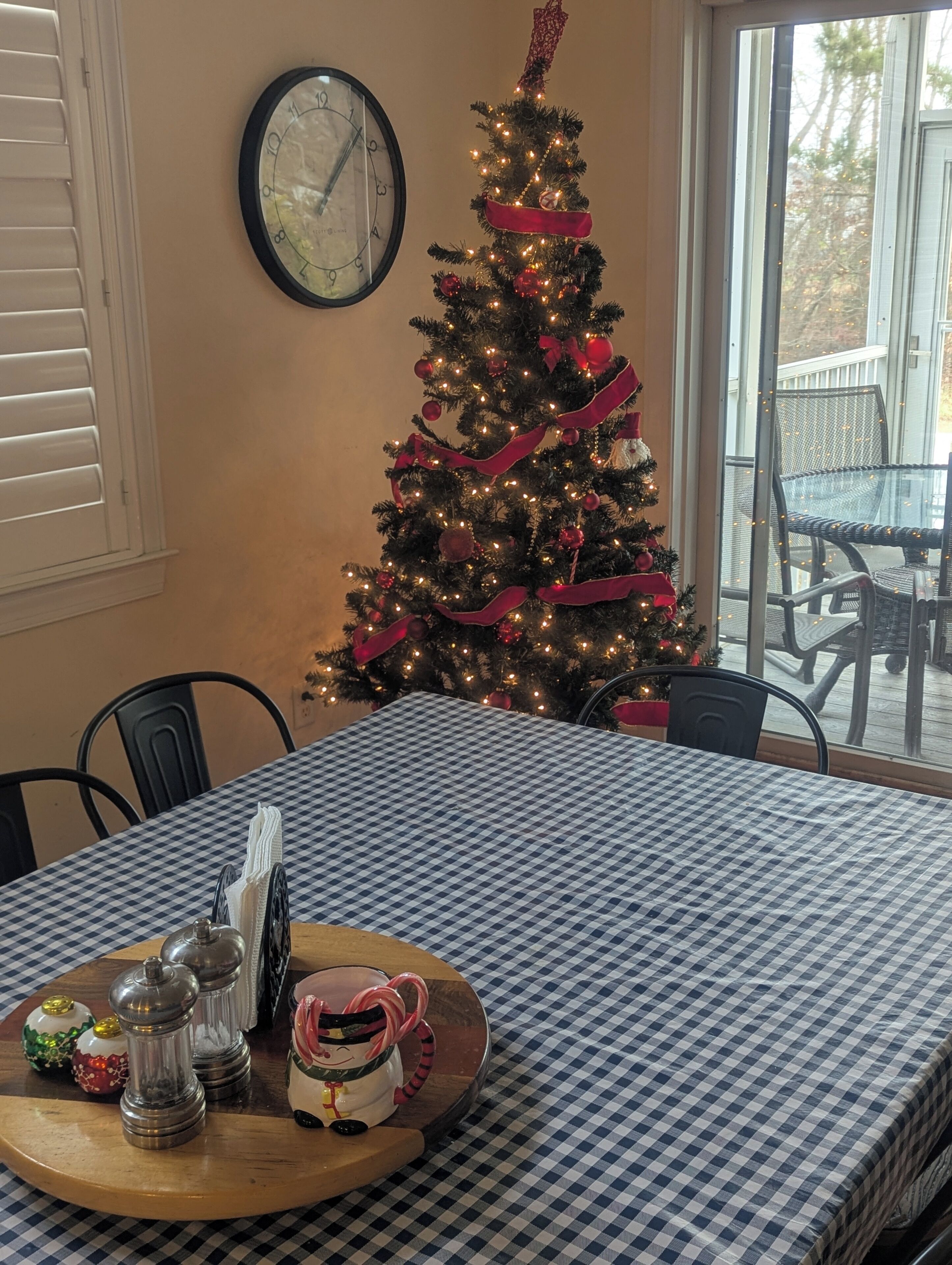 A dining area with a checkered tablecloth, a Christmas tree, salt and pepper shakers, and a clock on the wall.