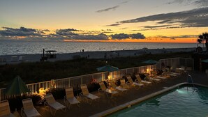 A poolside area with lounge chairs and umbrellas, overlooking a beach and the ocean at sunset. - TOP RATED / HUGE Balcony Beachfront 3 bed / 3 bath! (Panama City Beach)