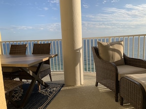 Enjoy the ocean view from this balcony with a table, chairs, and a wicker armchair.