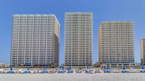 Three high-rise hotels with balconies, a beach in the foreground, and blue umbrellas. - TOP RATED / HUGE Balcony Beachfront 3 bed / 3 bath! (Panama City Beach)