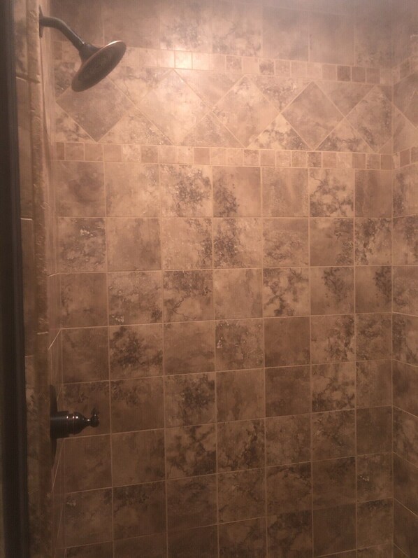 Un baño con ducha, paredes de azulejos y cabezal de ducha visible.