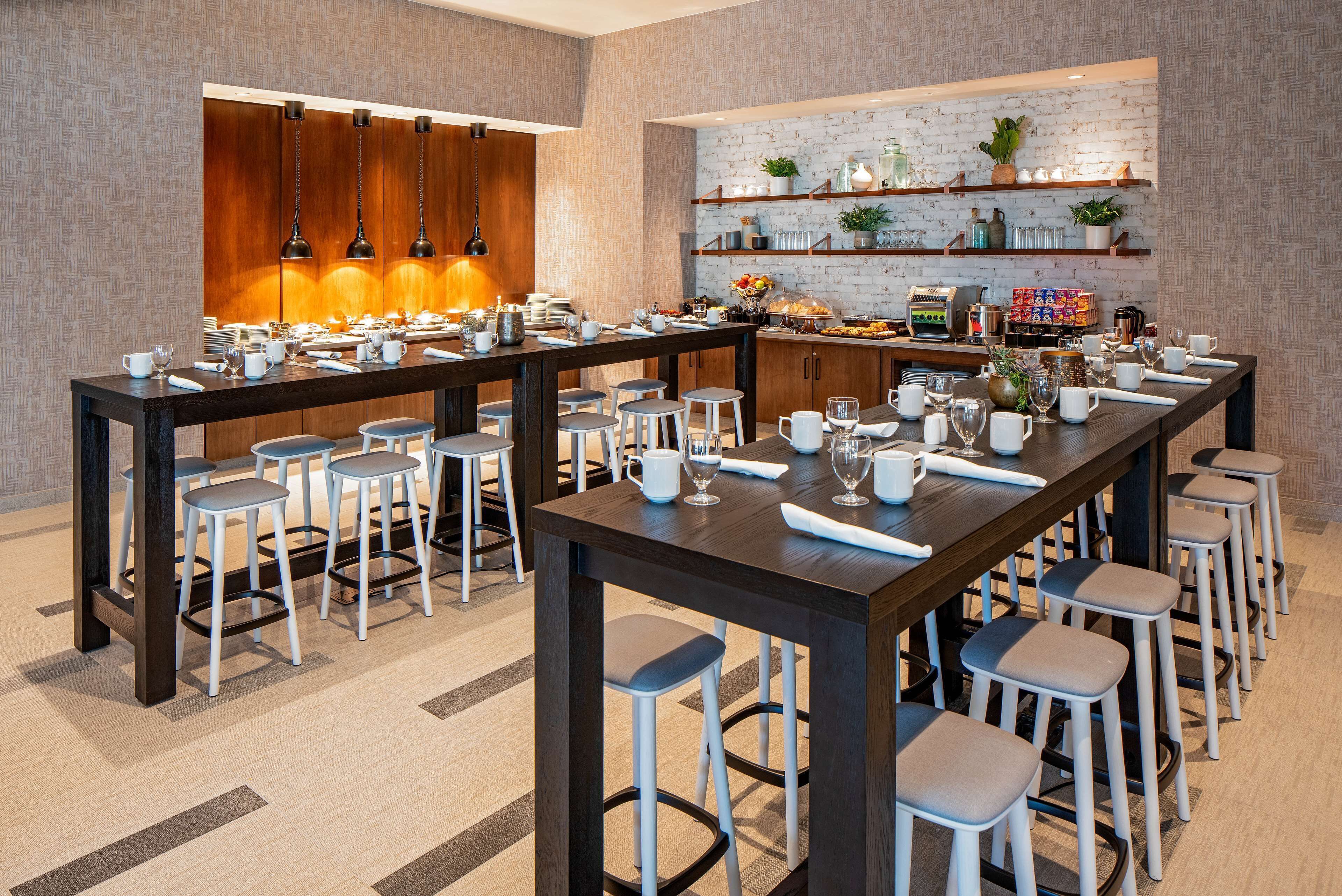 A modern dining area with a long table, multiple bar stools, and a variety of dining ware.