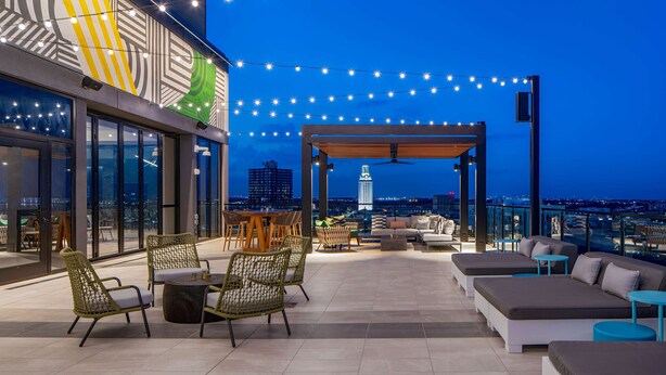 An outdoor terrace with seating, string lights, and a view of the city skyline.