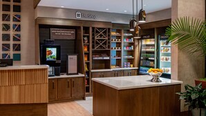 A modern coffee shop interior with wooden cabinetry, a central island with a bowl of fruit, and shelves stocked with various beverages.