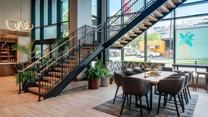 A modern interior with a staircase, wooden flooring, a dining area with chairs, and large windows.