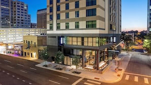 A modern hotel with a glass facade, a parking garage, and a street view.