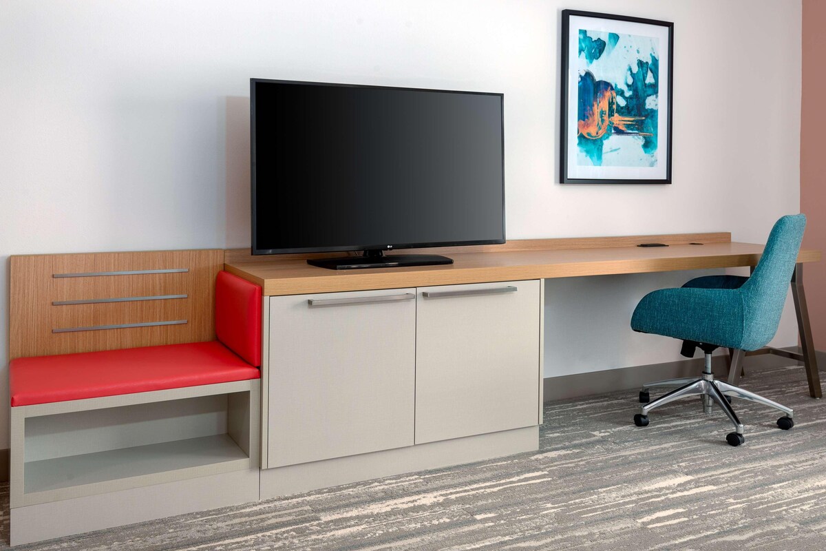 A modern office space with a desk, chair, TV, and a framed artwork on the wall.