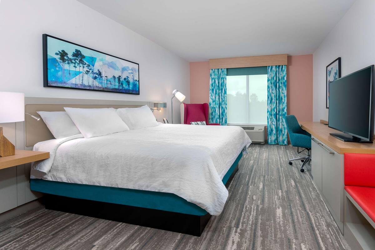 Une chambre d’hôtel avec un grand lit, un bureau avec une télévision, une chaise et une fenêtre avec des rideaux.