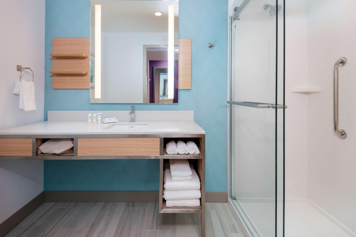 A modern bathroom with a large mirror, a sink, and a glass shower enclosure.