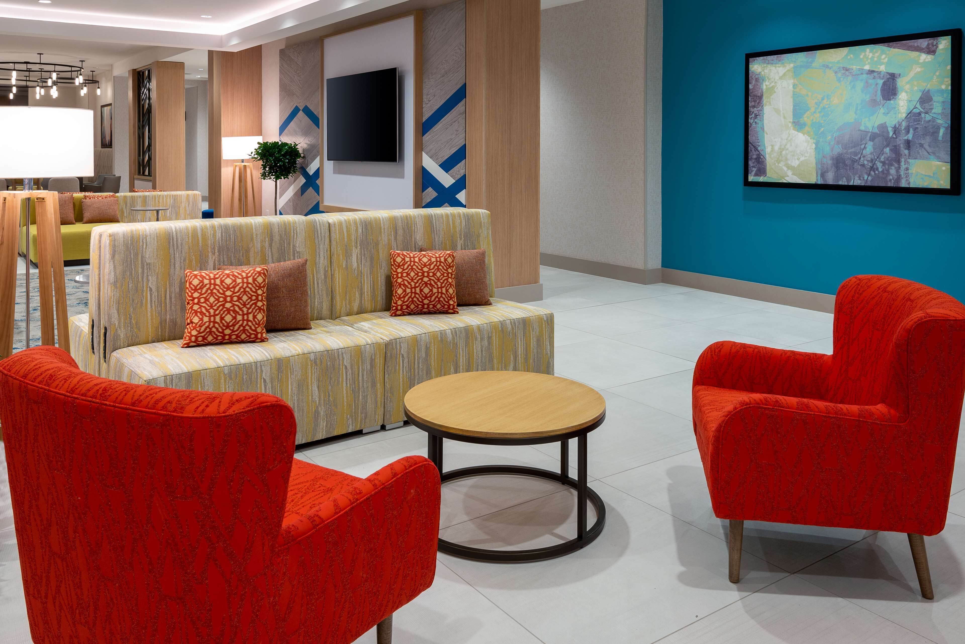 A modern lobby with a sofa, two armchairs, a round table, and a TV on the wall.