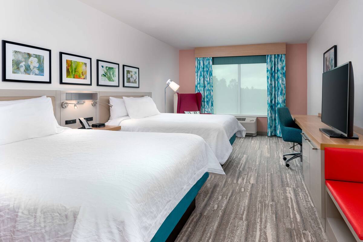 Une chambre d’hôtel avec deux lits, un bureau, une télévision et une fenêtre avec des rideaux.