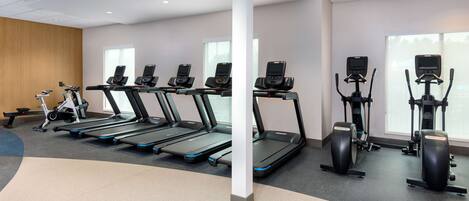 Un gimnasio con cintas de correr, elípticas y una bicicleta estática.