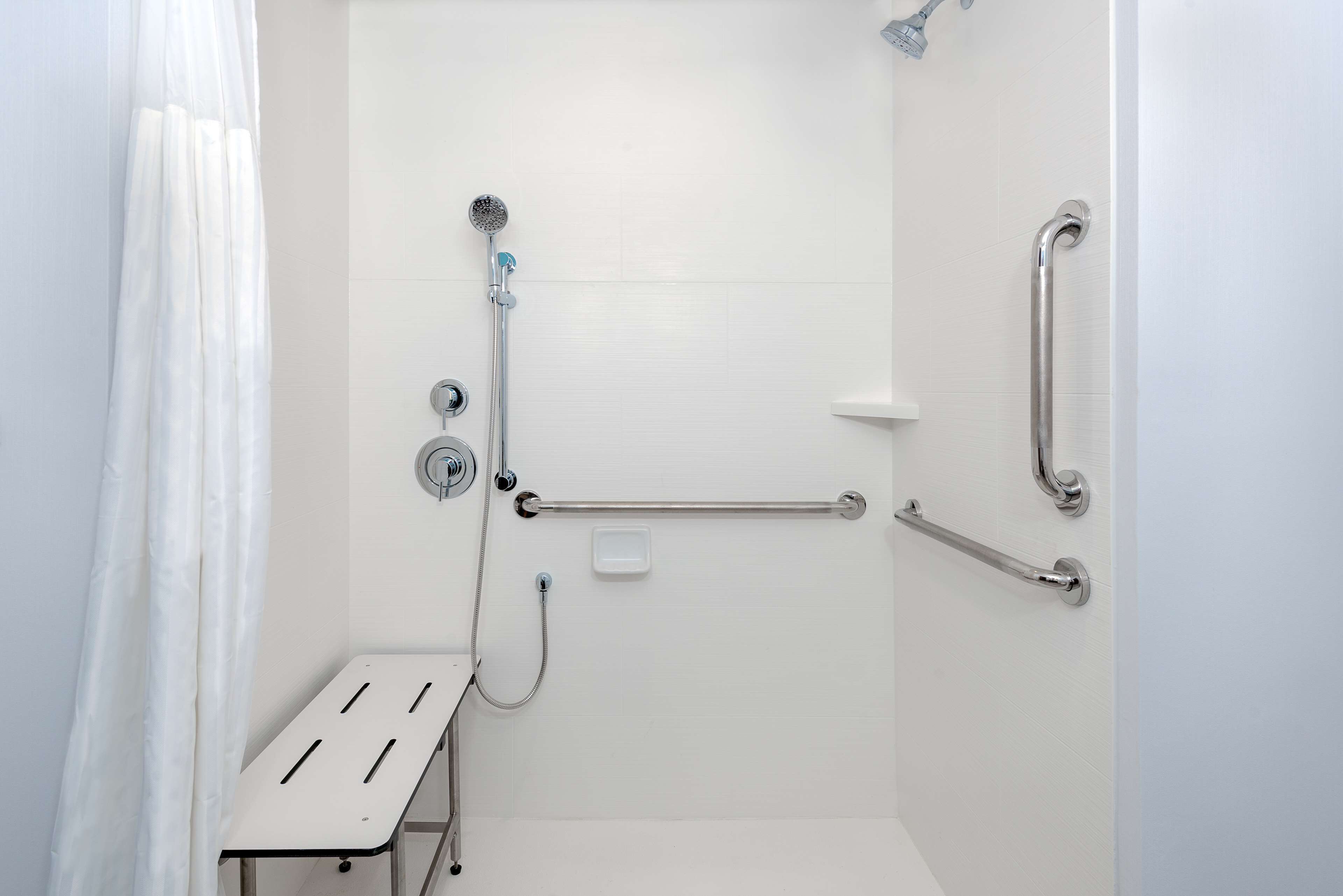 A bathroom with a shower, grab bars, and a white bench.