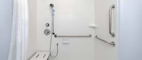A bathroom with a shower, grab bars, and a white bench.