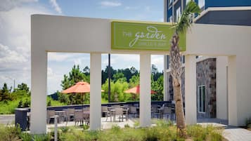 Ett utomhusområde med sittplatser, bord och stolar, en palmpalm och en skylt med texten ”The Garden Grille & Bar”.