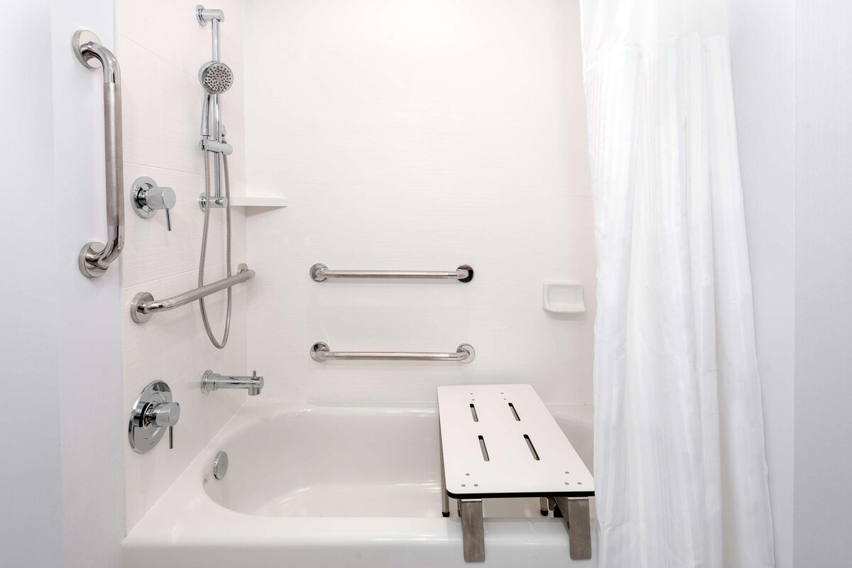 A modern bathroom with a bathtub, grab bars, and a shower head.
