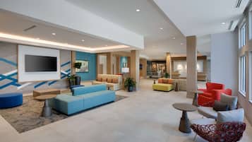 Een ruime lobby met een blauwe bank, rode stoelen en een moderne eetruimte.