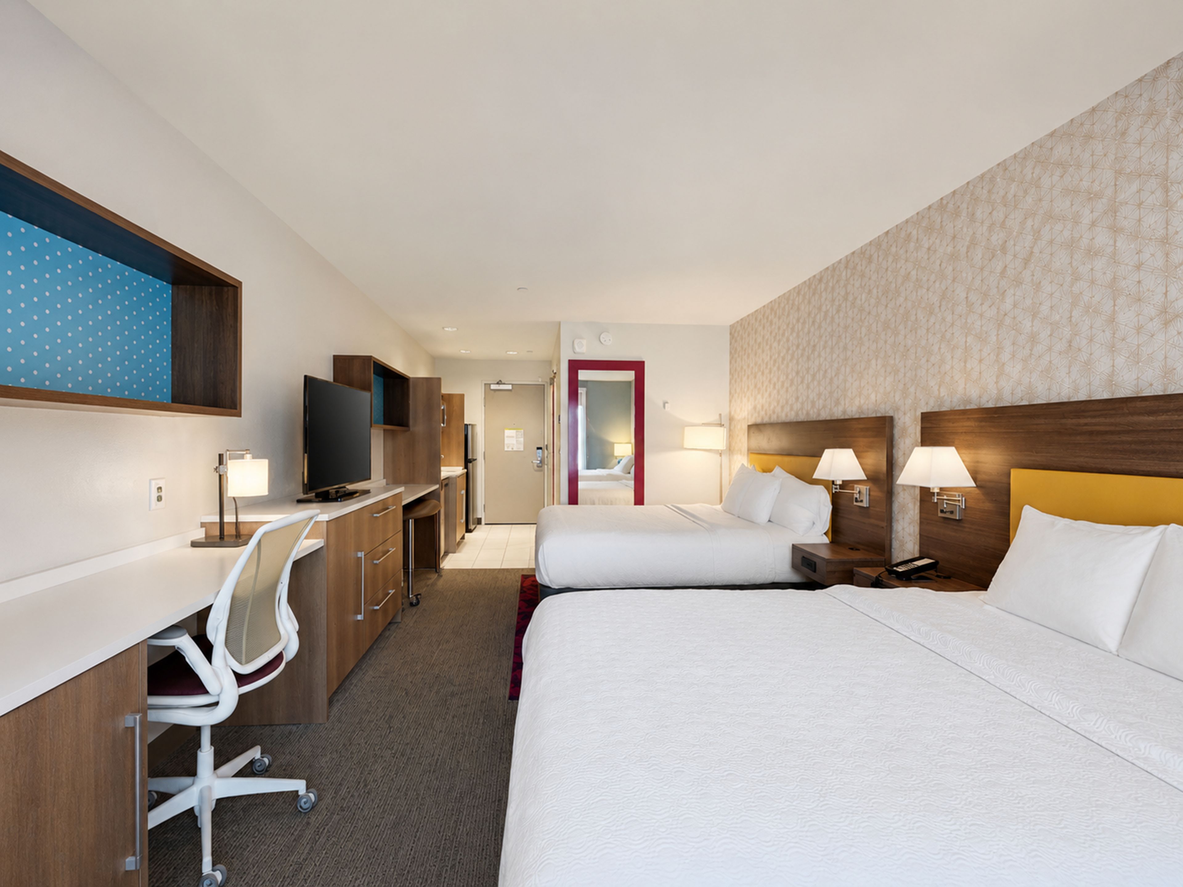 Une chambre d’hôtel équipée d’un lit, d’un bureau, d’une chaise, d’une télévision et de lampes de chevet.