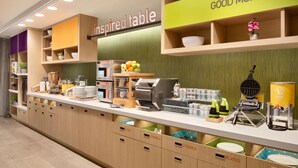Un área de cocina moderna con una barra desayunadora, identificada como 'inspired table', y un cartel con la frase 'BUENOS DÍAS' sobre el mostrador.