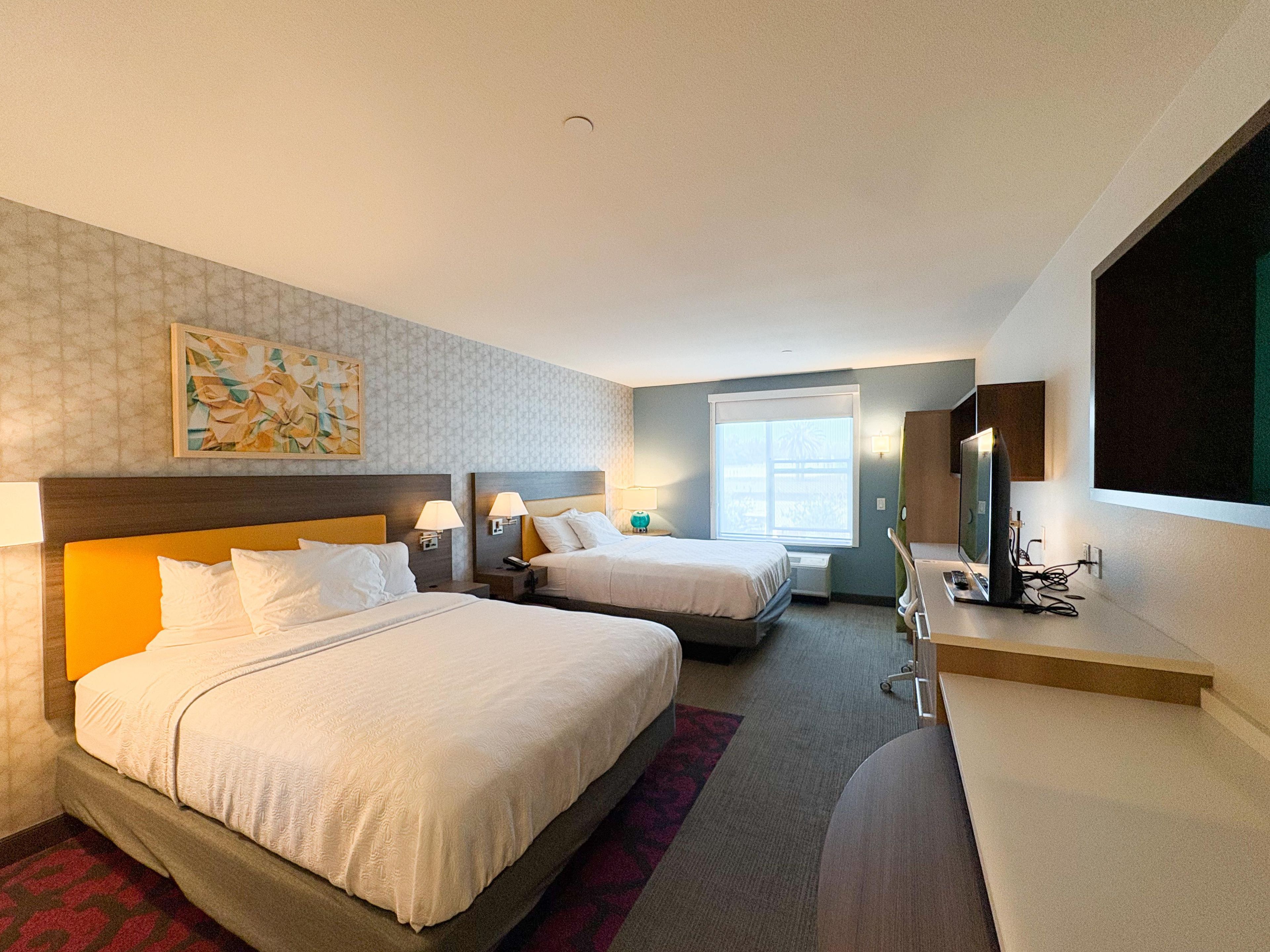 Habitación de hotel con dos camas, un escritorio, un televisor y una ventana.