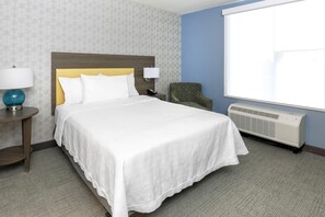 Una habitación de hotel con cama, mesita de noche, lámpara, silla y ventana.