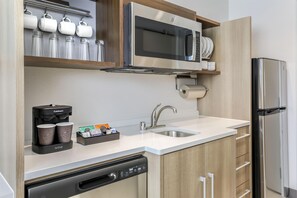 Una cocina moderna con lavavajillas integrado, cafetera, microondas y refrigerador de acero inoxidable.