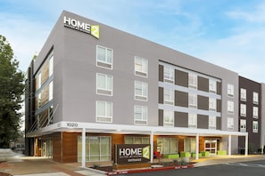 Een modern hotelgebouw met een bord waarop 'HOME 2 Suites by Hilton' staat en een 'Geen Parkeren'-bord bij de ingang.