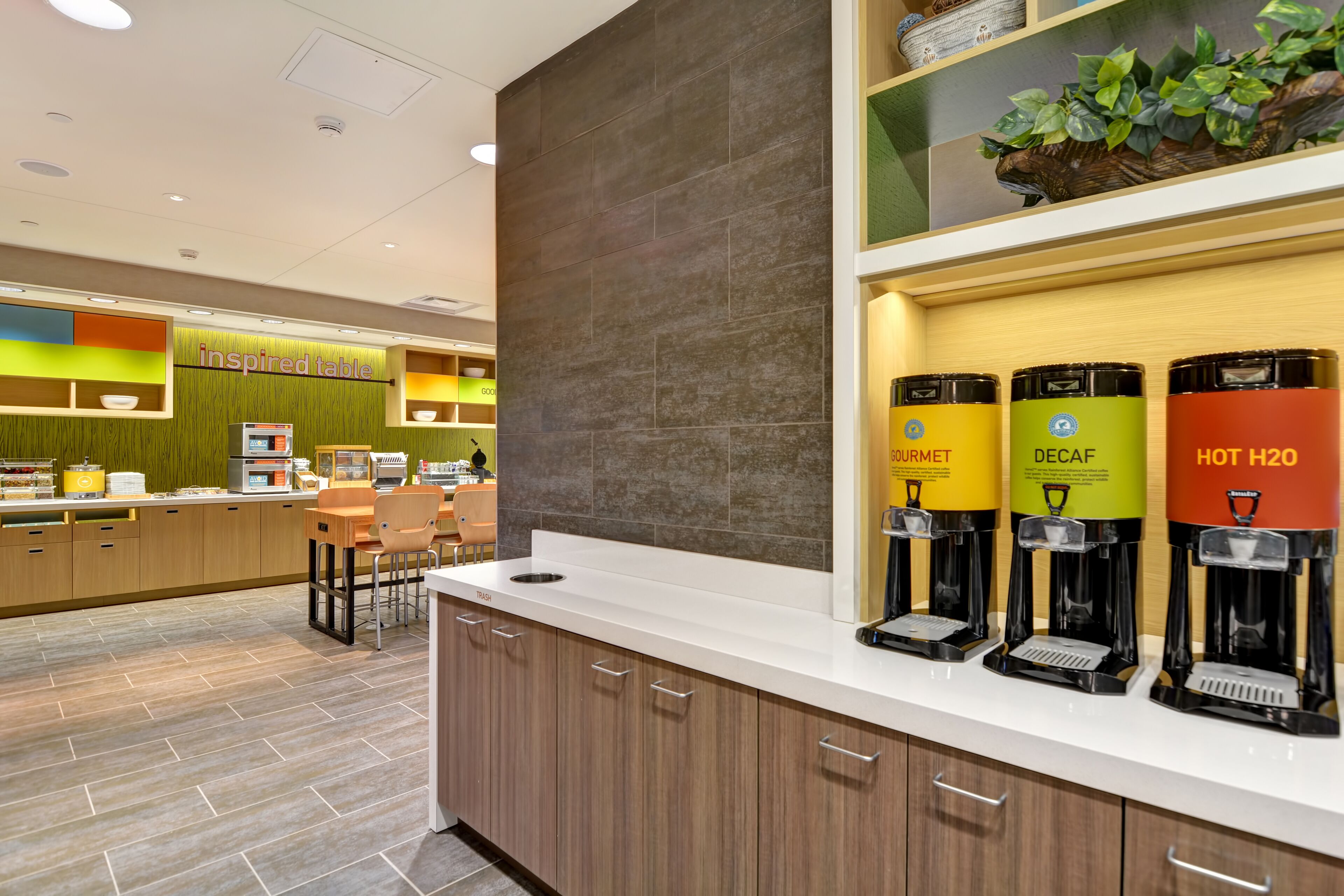 Un área de cocina moderna con estación de café que incluye dispensadores etiquetados para 'Bourmet', 'Descafeinado' y 'Agua Caliente'.