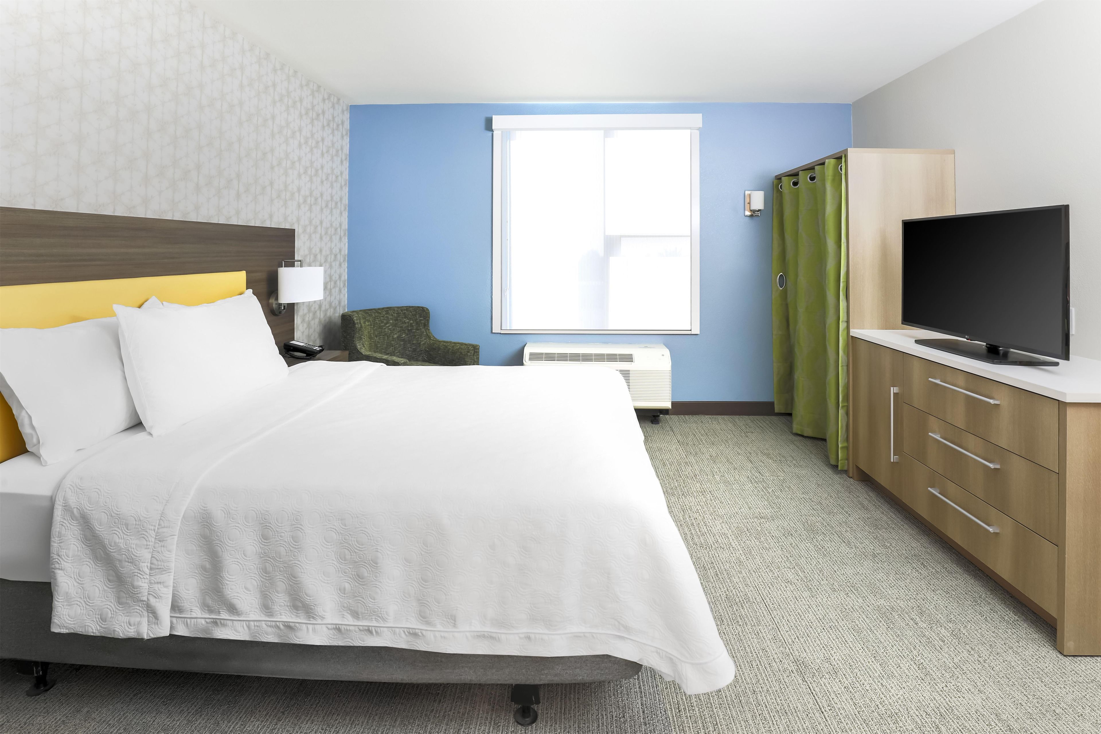 A hotel room with a bed, a TV, a desk, and a window.