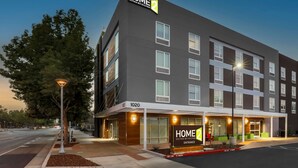 Un moderno edificio de hotel con un cartel que dice "HOME 2 Suites by Hilton" y una entrada visible.