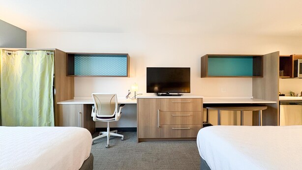 Une chambre d’hôtel avec deux lits, un bureau avec une chaise, une télévision et une petite kitchenette.
