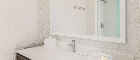 A bathroom with a white sink, a mirror, and a towel dispenser.