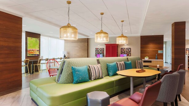 Un área de descanso moderna con un sofá verde, cojines estampados y una mesa redonda de madera con sillas.