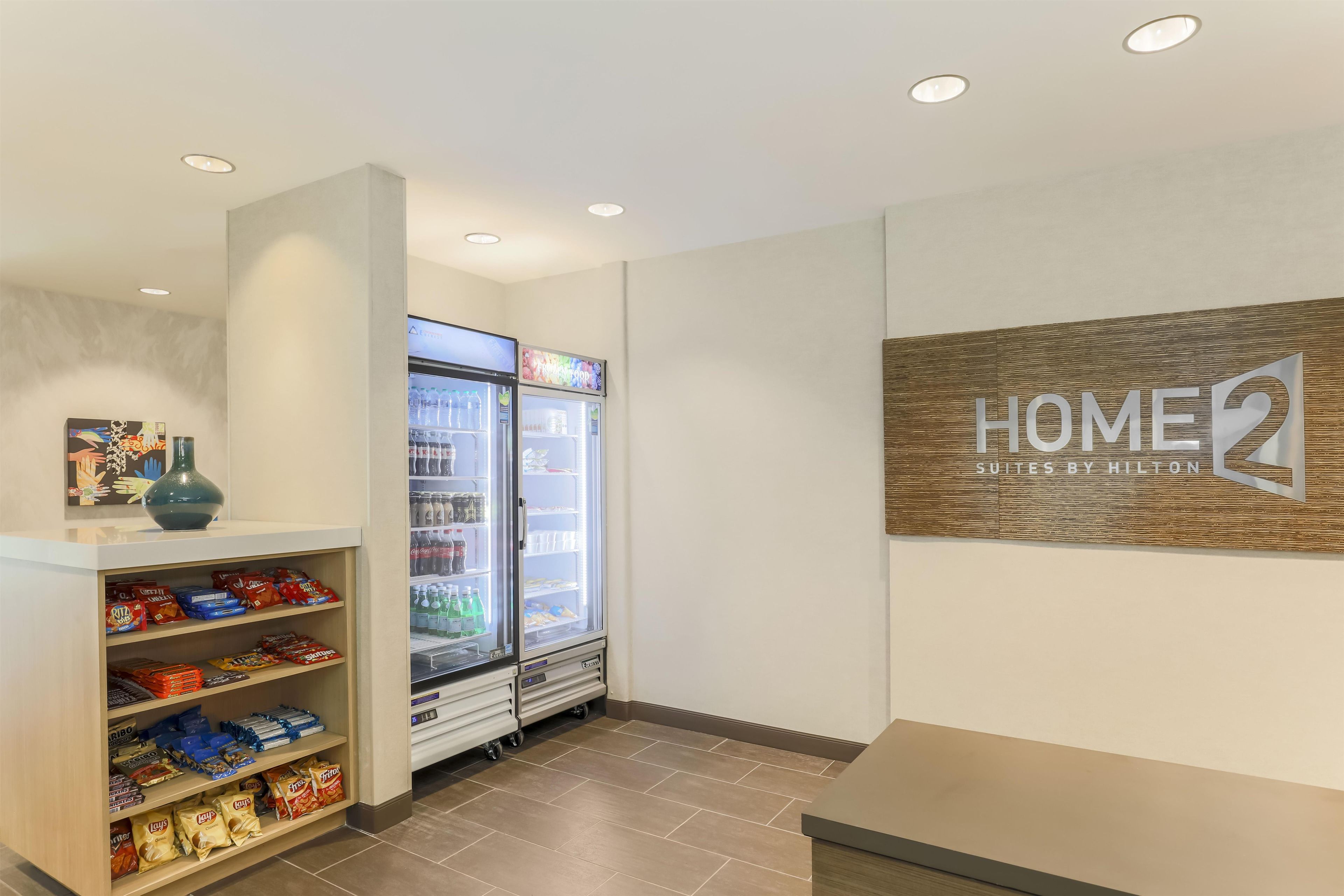 A hotel lobby with a vending machine, snack shelves, and a sign for 'HOME2 Suites by Hilton'.