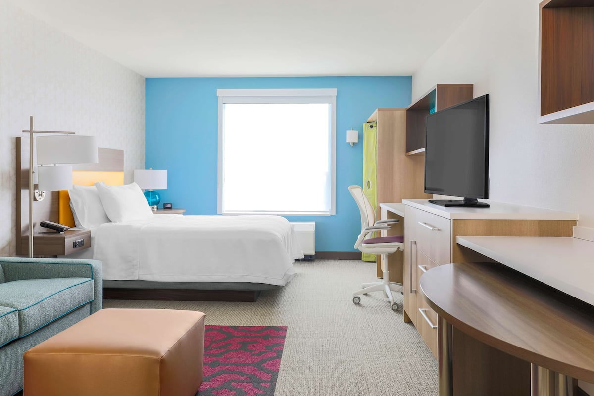A hotel room with a bed, a desk, a television, a chair, and a nightstand.