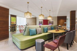 Un espace détente moderne avec un canapé vert, des coussins à motifs et une table ronde.