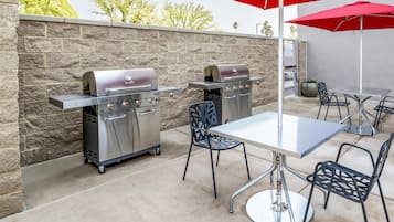 Patio esterno con due barbecue Char-Broil in acciaio inossidabile, un tavolo, sedie e un ombrellone rosso.