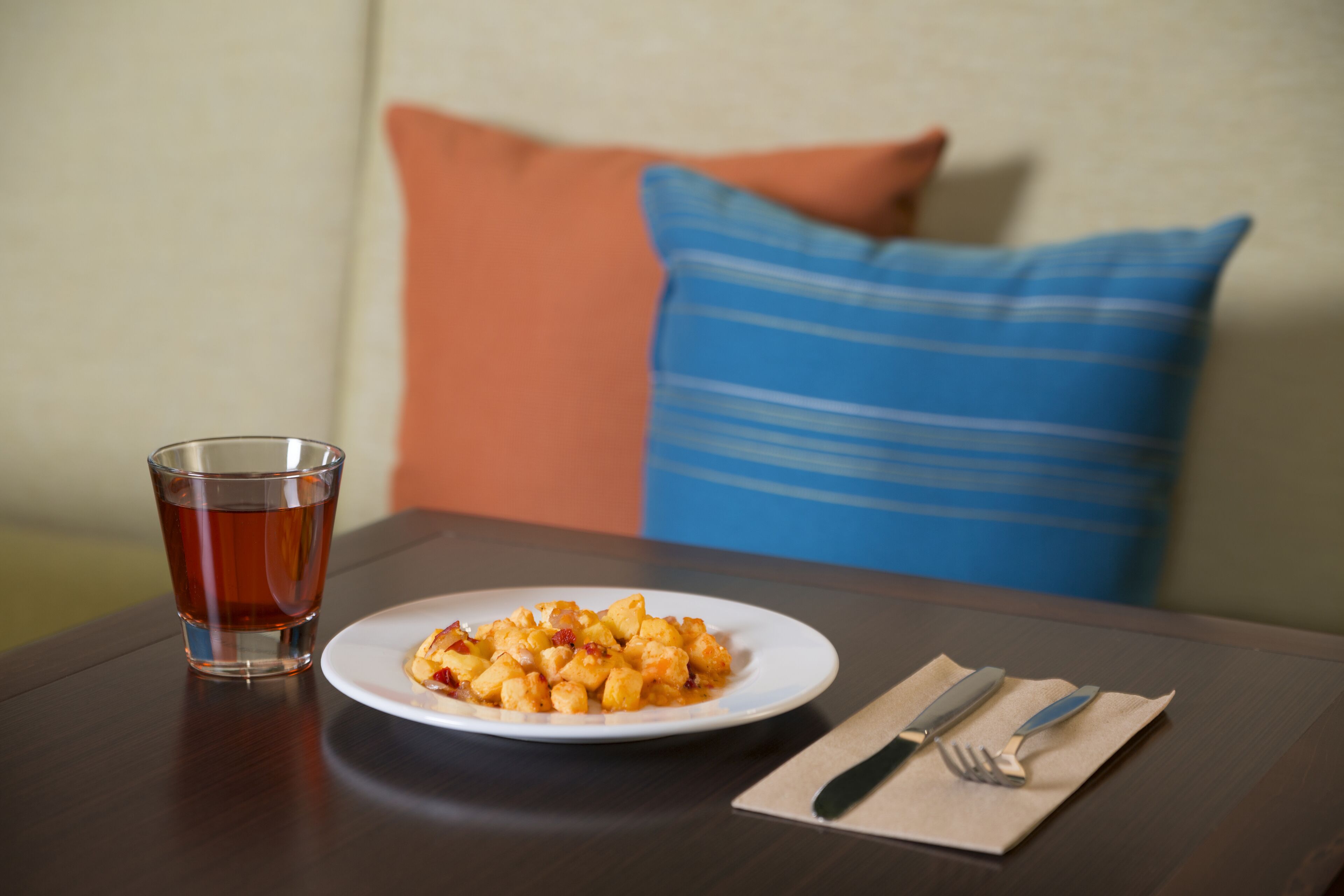A dining table with a plate of food, a glass of tea, and cutlery on a napkin.