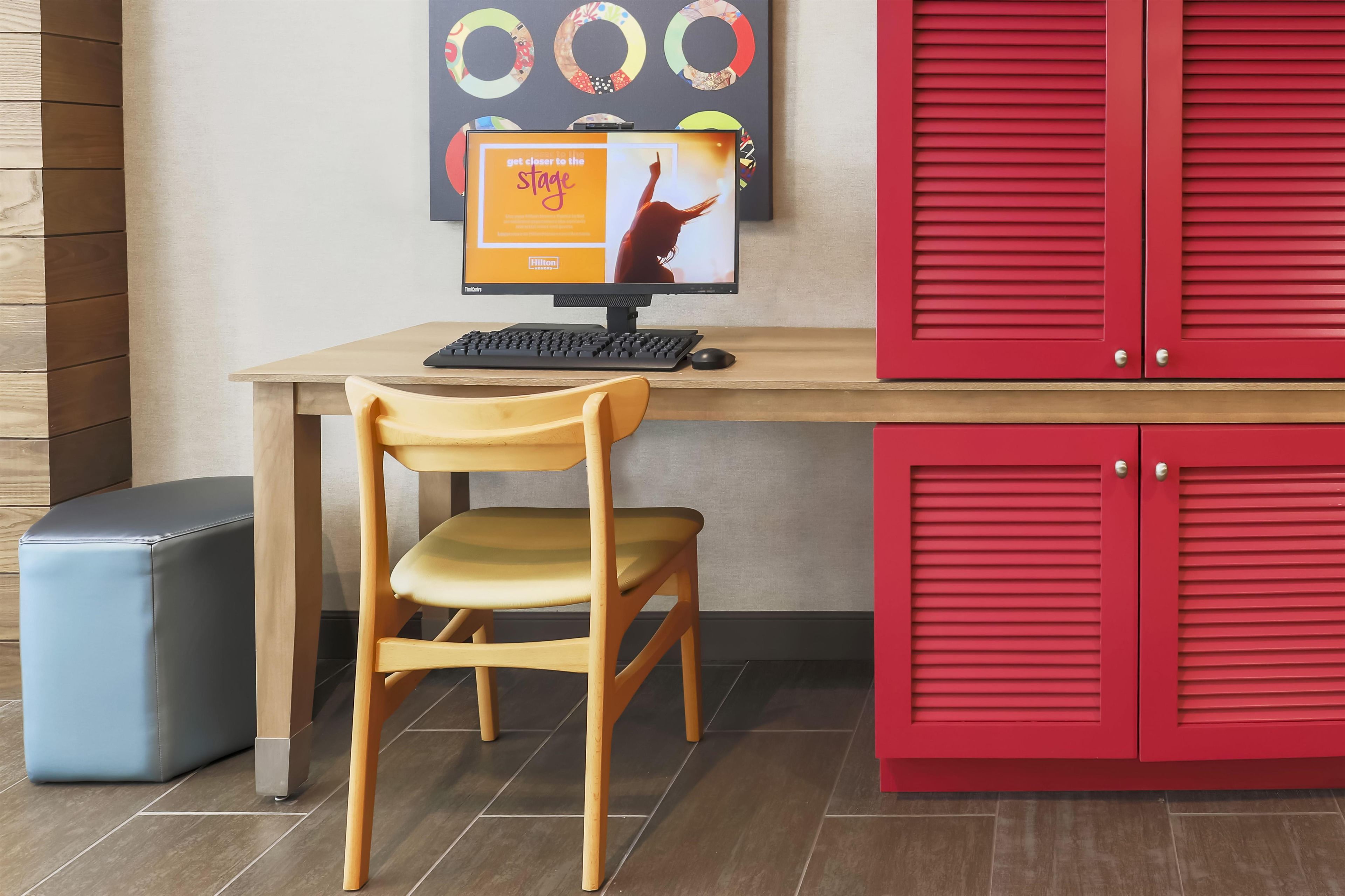 A hotel room with a wooden desk, a computer, a chair, and red storage cabinets.