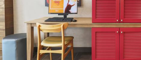 A hotel room with a wooden desk, a computer, a chair, and red storage cabinets.