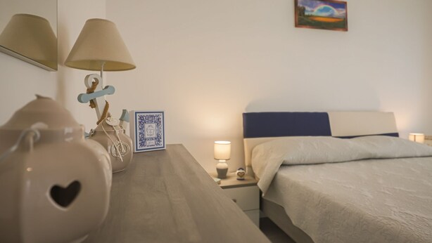 Un dormitorio con cama, mesitas de noche, lámparas, un jarrón decorativo, un cuadro enmarcado y una pintura en la pared.