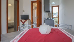 Un comedor con una mesa dispuesta para dos, una silla blanca, un mantel rojo y un hervidor blanco.