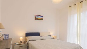 A bedroom with a bed, bedside tables, a lamp, a picture frame, and a window with curtains. - Apartment in Capaccio ID 3888 (Licinella-Torre di Paestum)