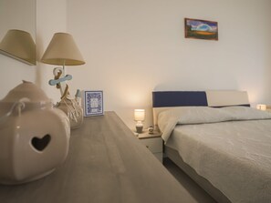 Un dormitorio con una cama, lámparas de noche, una mesita de noche, un jarrón decorativo, un cuadro enmarcado y una pintura en la pared.