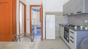 A modern kitchen with a refrigerator, stove, and sink. There is a dining table with chairs and a door leading to another room. - Appartament in Capaccio 4031 (Licinella-Torre di Paestum)